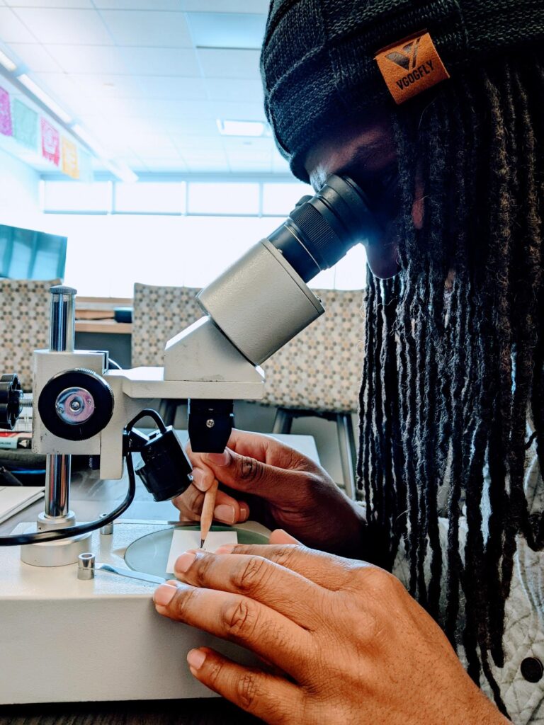 A person is looking through the eyepiece of a microscope at a paper they are drawing on.